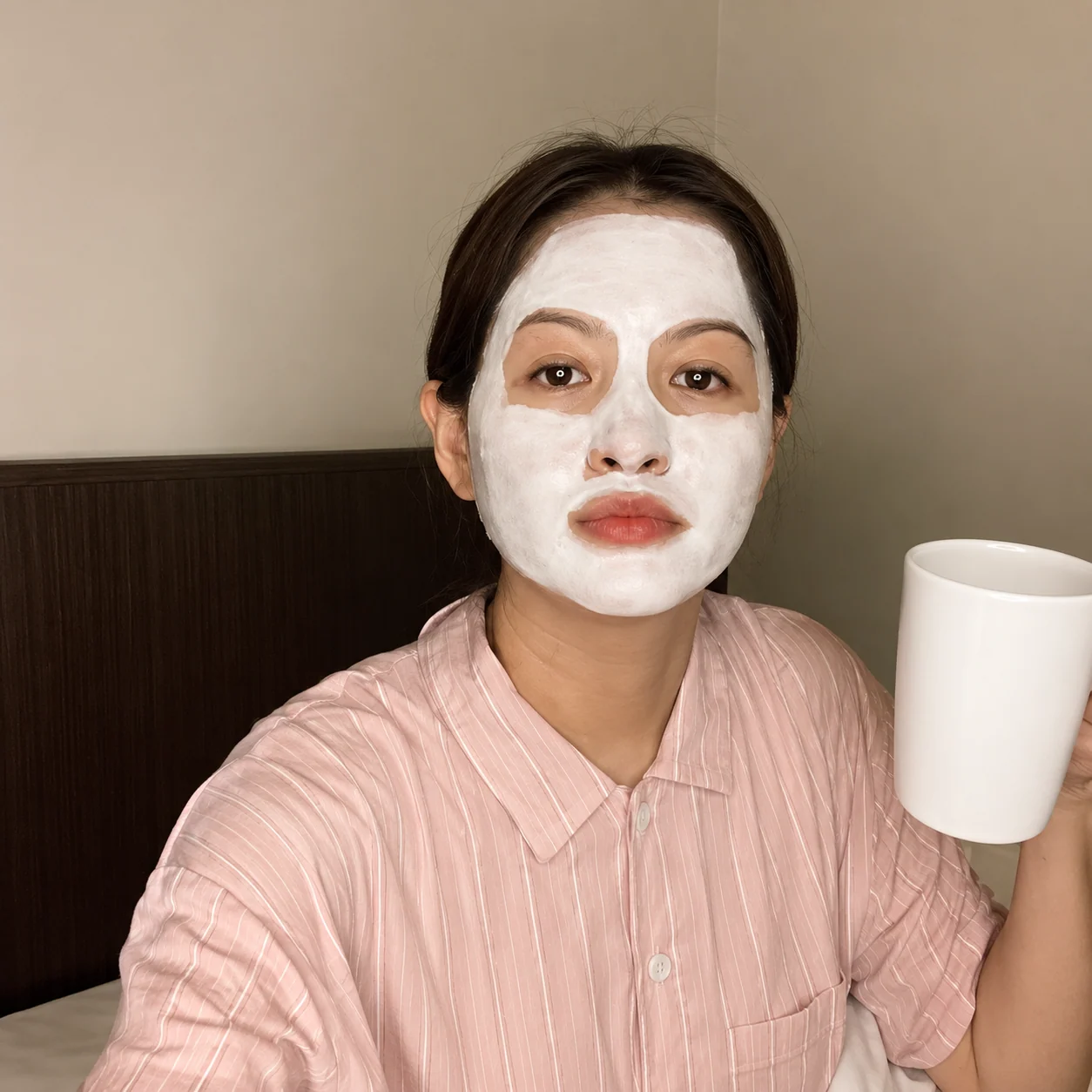 Customer wearing a light-colored clay mask while holding a cup